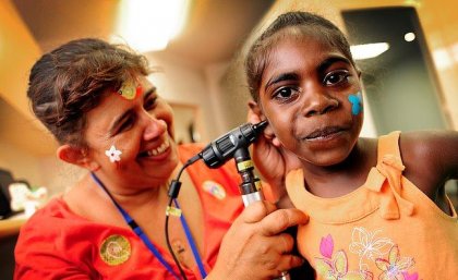 A health practitioner checks the ear of a young Indigenous girl.